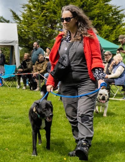 A woman and a black dog are walking into a dog show ring together